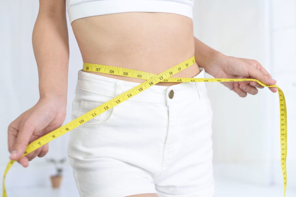 A woman is holding a measuring tape around her waist.